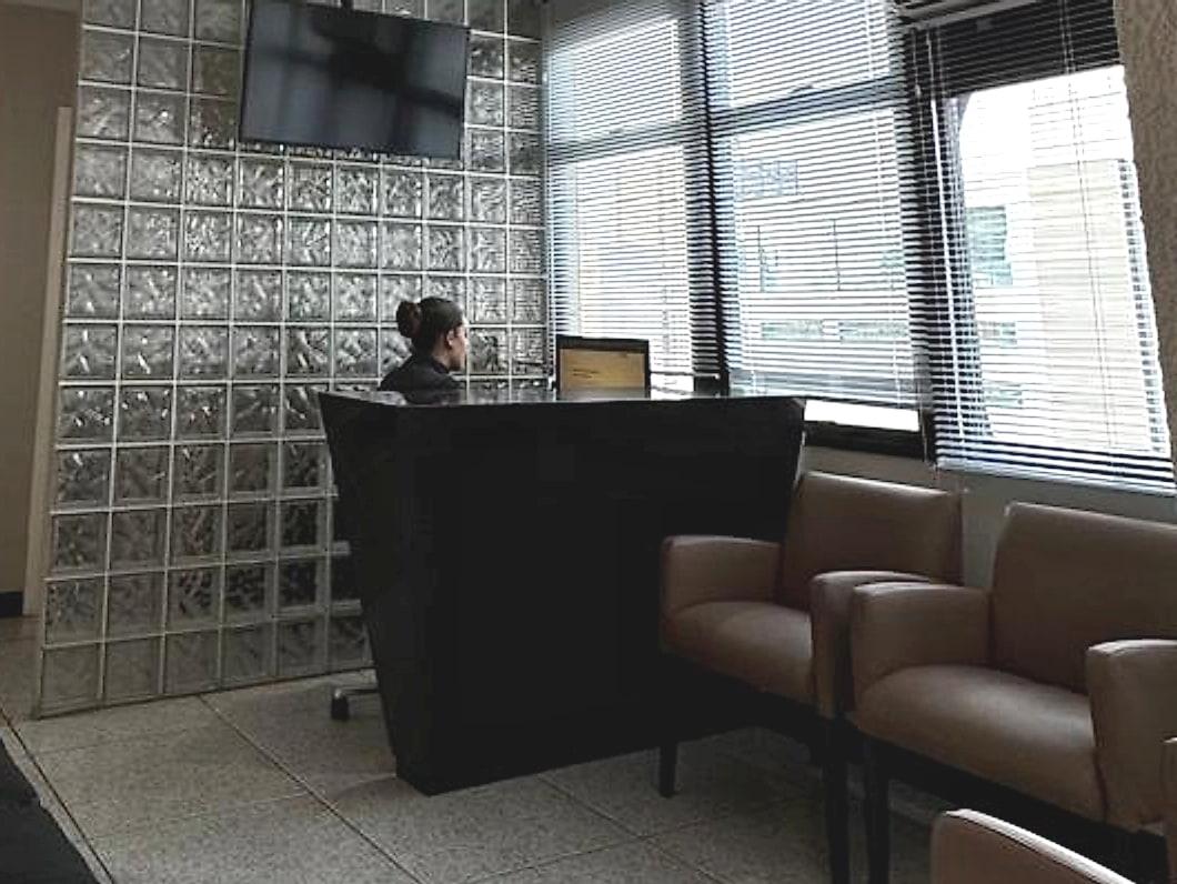 Recepção da J & R Odontologia, com balcão de atendimento, parede de blocos de vidro e poltronas da sala de espera
